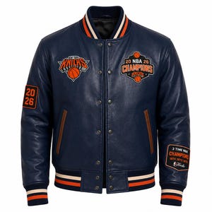 Pode incluir: Uma jaqueta varsity azul-marinho com punhos e gola canelados em listras laranja e brancas. A frente exibe um logotipo do New York Knicks e um emblema 20 NBA 26 Champions. As mangas incluem o texto 20 26 e 3 Time NBA Champions 1970 1973 1976.