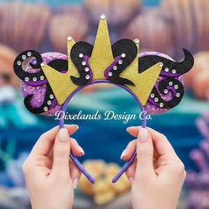 May include: A purple headband with a gold crown and black tentacles design. The headband features purple sequins and is embellished with rhinestones. The text "Dixelands Design Co." is visible on the headband.