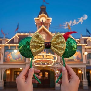 May include: Green sequined mouse ears with a gold sequined bow and a red feather. The ears are held up in front of a building with the words "Peter Flights" and "Dixielands Design Co."