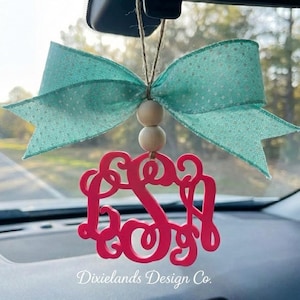 Puede incluir: Un ambientador para coche con un lazo turquesa y un monograma rosa. El lazo tiene un estampado de lunares blancos. El monograma es una letra "S" en cursiva. El texto "Dixielands Design Co." está en la parte inferior.