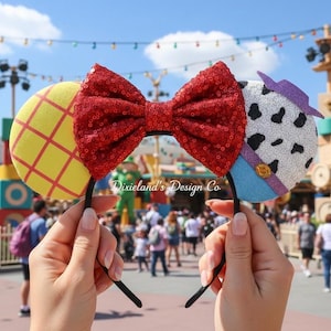 May include: Black headband with themed ears and a red sequin bow. One ear is yellow with a red grid, the other is white with black spots and a purple hat. A fun accessory.