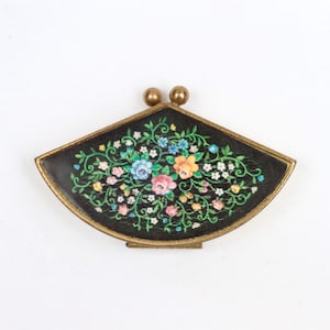 Pode incluir: Um estojo compacto em forma de leque com fundo preto, apresentando um padrão floral colorido de flores rosas, azuis, amarelas e brancas com vinhas verdes. O estojo tem uma moldura de metal dourado e um fecho de duas esferas no topo.