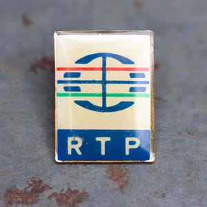 May include: Rectangular pin with a cream-colored background, featuring a blue globe design with red, green, and blue horizontal lines. The letters "RTP" are in blue at the bottom. The pin has a gold-colored border.