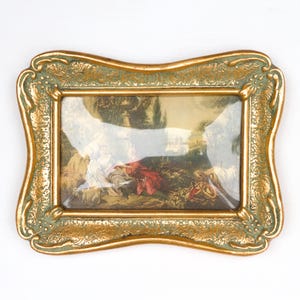 May include: A rectangular picture frame with a decorative, ornate border featuring a gold and sage green finish. The frame encloses a print depicting a landscape scene with figures in period clothing, including a person in a red garment.