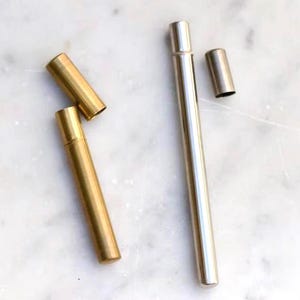 以下が含まれることがあります： マットゴールド仕上げとポリッシュシルバー仕上げの2つの円筒形金属ケース。各ケースは長いチューブと取り外し可能なキャップで構成されています。ゴールドのケースは短く、シルバーのケースはより長くスリムな形状をしています。