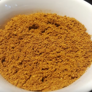 May include: A white bowl filled with a mound of brown spice powder.