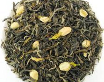 May include: A close-up of loose leaf green tea with white jasmine flower buds. The tea is a blend of green tea leaves and white jasmine flowers.