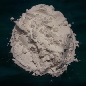 May include: A close-up of a pile of white powder on a teal surface. The powder is finely ground and has a smooth texture.