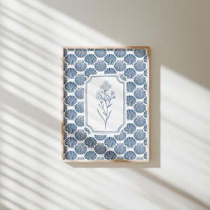 Puede incluir: Una impresión artística enmarcada con un fondo de patrón de conchas marinas azules y blancas. El centro tiene un rectángulo blanco con una ilustración floral azul. El marco es de color madera clara.