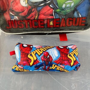 May include: A blue pencil case featuring the Marvel character Spider-Man. The case has a red zipper pull and a repeating pattern of Spider-Man in action poses. The top of the image shows a Justice League lunchbox.