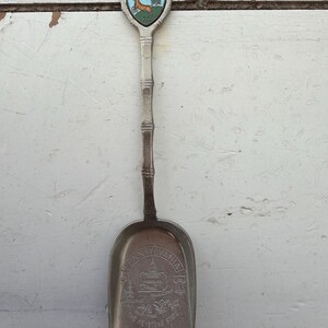 May include: Vintage Pocono Mountains souvenir spoon. The spoon features a shield-shaped emblem with a deer and tree, and the words "Pocono Mountains". The scoop has an image of a building and the words "Pennsylvania, The Keystone State".