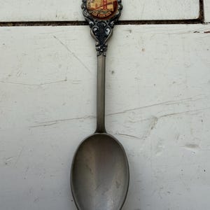 May include: A vintage silver-coloured souvenir spoon. The spoon features an image of the Golden Gate Bridge in San Francisco on the handle, with the words "Golden Gate Bridge San Francisco".
