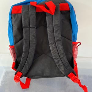 May include: A blue, red, and black backpack with adjustable red straps and mesh side pockets. The backpack has a padded back panel and shoulder straps for comfort. The top of the backpack is red, and the bottom is black.