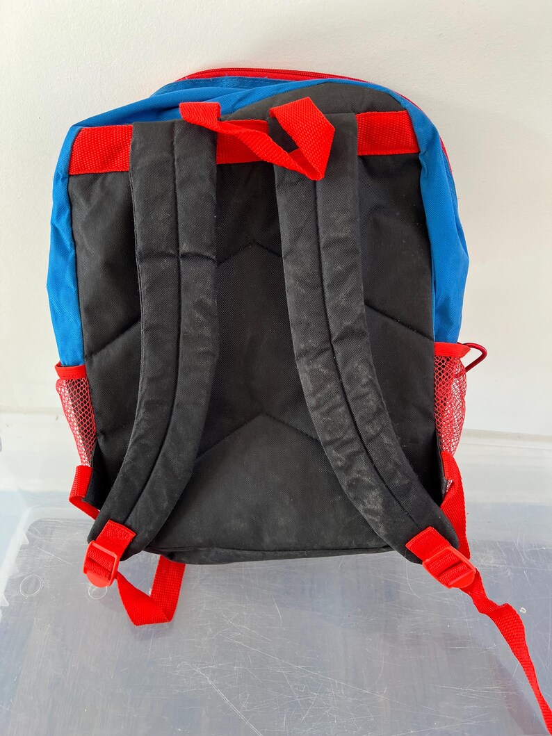 May include: A blue, red, and black backpack with adjustable red straps and mesh side pockets. The backpack has a padded back panel and shoulder straps for comfort. The top of the backpack is red, and the bottom is black.