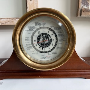 Könnte beinhalten: Eine Vintage Seth Thomas Weltzeituhr mit einer Messinglünette und einem dunklen Holzsockel. Das Zifferblatt zeigt eine Weltkarte und Zeitzonen an. Die Uhr ist ein dekorativer Artikel.