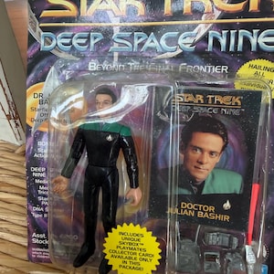 May include: A Star Trek Deep Space Nine action figure of Doctor Julian Bashir in a black and teal uniform, sealed in original packaging with a collector card and accessories, featuring the text Star Trek Deep Space Nine and Doctor Julian Bashir.