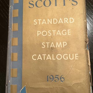 Könnte beinhalten: Ein Vintage Scott's Standard Briefmarkenkatalog von 1956. Das Cover ist beige mit blauen Akzenten und der Titel in großen, fetten Buchstaben. Das Cover weist Gebrauchsspuren auf.