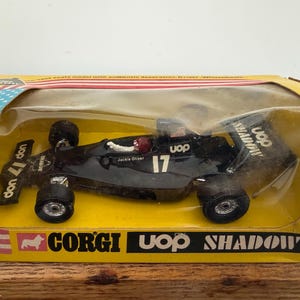 Puede incluir: Modelo de coche de carreras Corgi UOP Shadow negro en su caja amarilla original. El coche tiene el número 17 en el lateral y el alerón trasero, con "Jackie Oliver" impreso en el lateral. La caja tiene una ventana de plástico transparente.