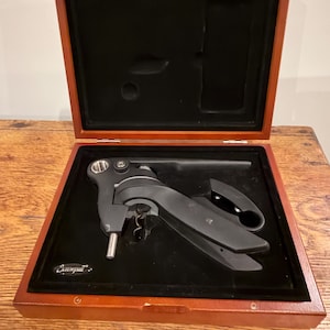 May include: A black Screwpull corkscrew set in a wooden box with a black velvet interior. The box is open, revealing the corkscrew and its components. The wooden box has a reddish-brown finish.