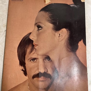 Könnte beinhalten: Vintage-Zeitschriften-Cover mit einem Mann und einer Frau in enger Umarmung. Die Frau hat dunkles Haar und ist im Profil, während der Mann den Betrachter direkt ansieht. Das Cover hat einen pfirsichfarbenen Hintergrund.