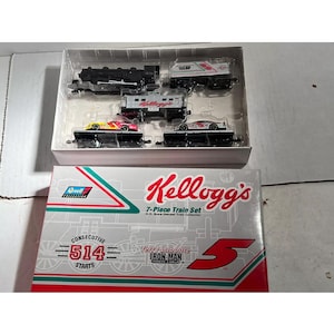 May include: A 7-piece Kellogg's train set in a clear plastic case, with a box featuring the Kellogg's logo and the text "7-Piece Train Set". The box also displays "Consecutive 514 Starts" and "Iron Man".