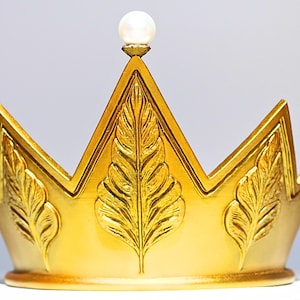 May include: A gold-colored crown with a pearl at the top. The crown has a series of points and is decorated with leaf-like designs. The crown is likely a decorative item or part of a costume.