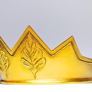 May include: A golden crown with a pearl at the top. The crown has a series of points and is decorated with leaf designs. The crown is made of a shiny gold material and is likely a decorative item.