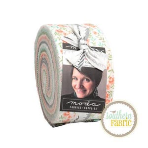 May include: A roll of fabric featuring a floral print in shades of pink, green, and white. The fabric is rolled up and tied with a white ribbon. The label on the fabric reads "moda fabrics + supplies".