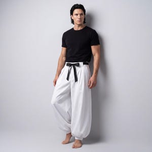 May include: A black crew neck t-shirt and white, wide-leg trousers with a black bow belt. The trousers have a distinctive, voluminous shape, with a gathered hem. The outfit is simple yet stylish, suitable for various occasions.