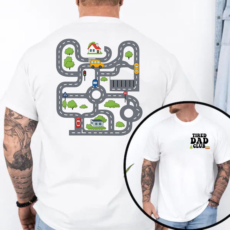 May include: White t-shirt featuring a colorful road map design on the back with cars, houses, and trees. The front of the shirt has the text "TIRED DAD CLUB" in black and green.