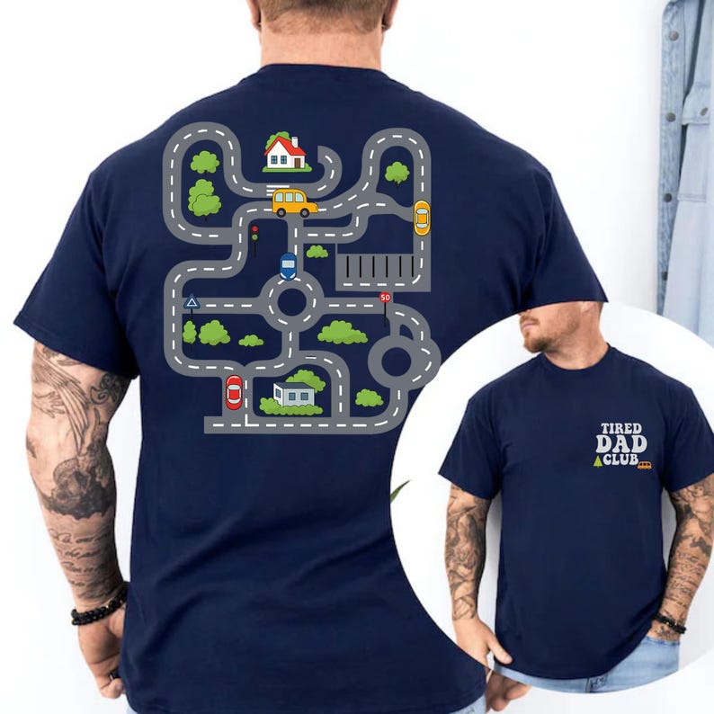 May include: Navy blue t-shirt featuring a road map design on the back with cars, houses, and trees. The front of the shirt has the text "TIRED DAD CLUB" in white and yellow.