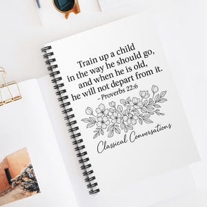 Könnte beinhalten: Ein weißes Spiralnotizbuch mit dem Text "Train up a child in the way he should go, and when he is old, he will not depart from it. - Proverbs 22:6" und "Classical Conversations". Eine goldene Büroklammer und eine Sonnenbrille sind ebenfalls zu sehen.