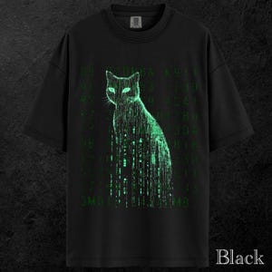 May include: Black t-shirt featuring a green cat design with a matrix-style pattern. The cat's silhouette is formed by lines of green code, with the word "Black" printed at the bottom. The shirt has a crew neck and short sleeves.