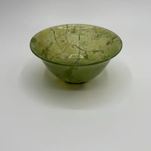 May include: A small, green jade bowl with a marbled pattern. The bowl is smooth and polished.
