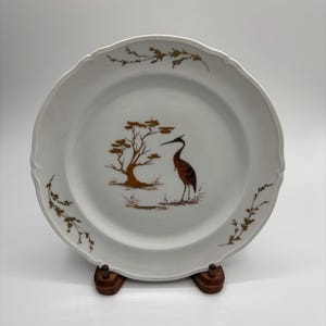 May include: White porcelain plate with a gold trim and a brown bird and tree design.