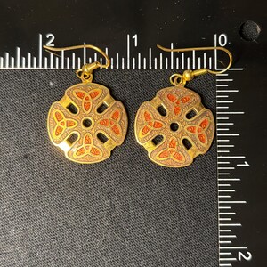 Könnte beinhalten: Ein Paar goldfarbene Ohrringe mit einem keltischen Knotendesign. Die Ohrringe sind mit rotem Email verziert und haben einen Hakenverschluss.