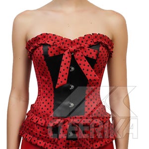 May include: A red corset with black polka dots and a black panel down the front. The corset features a bow and ruffle trim. The garment has a strapless design and is made of a shiny fabric.