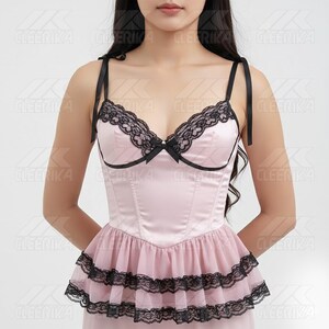 May include: A light pink corset top with black lace trim and a small bow. The top has thin black straps and a ruffled skirt with black lace. The corset is made of a satin-like material.