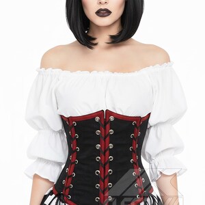 May include: A black corset with red edging and lacing, worn with a white off-the-shoulder top and a black and white striped skirt. The corset has silver eyelets, creating a gothic or steampunk style.