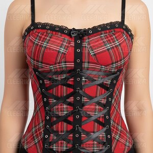 May include: Red plaid corset with black lace trim and a small bow. The corset features black ribbon lacing and thin black straps. The garment has a structured bodice with a classic plaid pattern. The corset is a stylish piece of apparel.