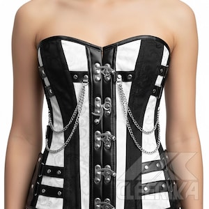May include: A black and white striped corset with silver metal clasps and chains. The strapless corset has vertical stripes and decorative detailing. The garment is made from a combination of materials, including leather and fabric.