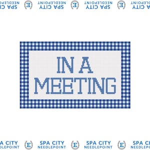 May include: A needlepoint design with the text "IN A MEETING" in blue letters on a white background. The design is framed by a blue and white gingham pattern. The words "SPA CITY NEEDLEPOINT" are printed around the border.