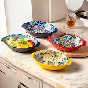 Puede incluir: Cuatro cuencos decorativos de cerámica con coloridos diseños florales. Los cuencos tienen forma ovalada con bordes festoneados y asas. Un cuenco contiene una ensalada con tomates y mango.