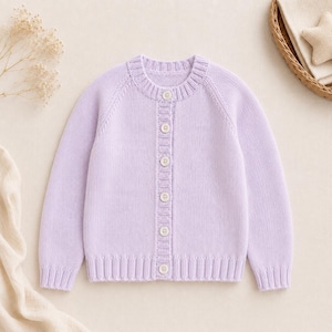 May include: A light lavender long-sleeve knit cardigan featuring a ribbed crew neckline, ribbed cuffs, and a ribbed hem. The garment is fastened down the center front with six small, round, light-colored buttons aligned vertically on a ribbed placket.