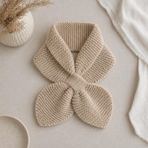 Puede incluir: Bufanda beige tejida con un diseño superpuesto único. Hecha de hilo suave y texturizado, la bufanda presenta una forma distintiva, ideal para añadir un toque de calidez y estilo. Su color neutro la hace adecuada para varios conjuntos.