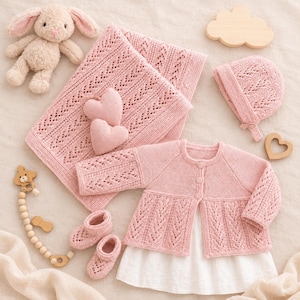 May include: A set of baby items including a light pink knitted blanket with a lace pattern, a matching long-sleeve cardigan, a bonnet, and booties. Also included are a plush bunny, two felt hearts, a wooden cloud, a heart, and a wooden bead toy.