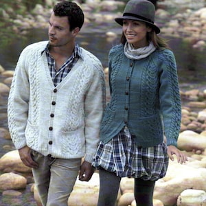 May include: A couple in knitted cardigans and plaid outfits. The man wears a cream cable-knit cardigan with dark buttons, and the woman wears a teal cardigan with a matching hat and scarf. They are near a rocky stream.