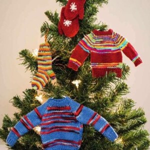 May include: A Christmas tree decorated with miniature knitted ornaments. The ornaments include a pair of red mittens, a striped sock, and two miniature sweaters in red and blue with colorful stripes. The ornaments are made of yarn.