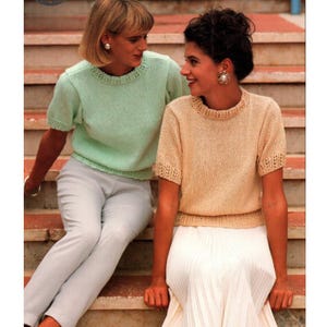 Puede incluir: Dos mujeres con tops de punto de manga corta. Uno es verde claro, el otro es beige. Ambos tops tienen un escote decorativo y mangas cortas. Una mujer lleva pantalones grises claros, la otra una falda blanca.