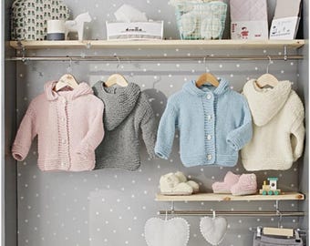 May include: A display of baby clothing in a closet. Pink, gray, light blue, and cream-colored knitted hooded cardigans hang on wooden hangers. Matching booties and a toy train sit on a shelf below. The closet has a gray background with white star patterns.